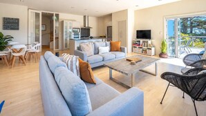 A modern living room with a sofa, coffee table, and TV. There is a balcony with outdoor furniture. - Hekerua Bay Retreat - Coastal Views (Waiheke Island)