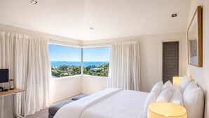A bedroom with a large bed, a desk with a computer, and a view of the sea. - Hekerua Bay Retreat - Coastal Views (Waiheke Island)