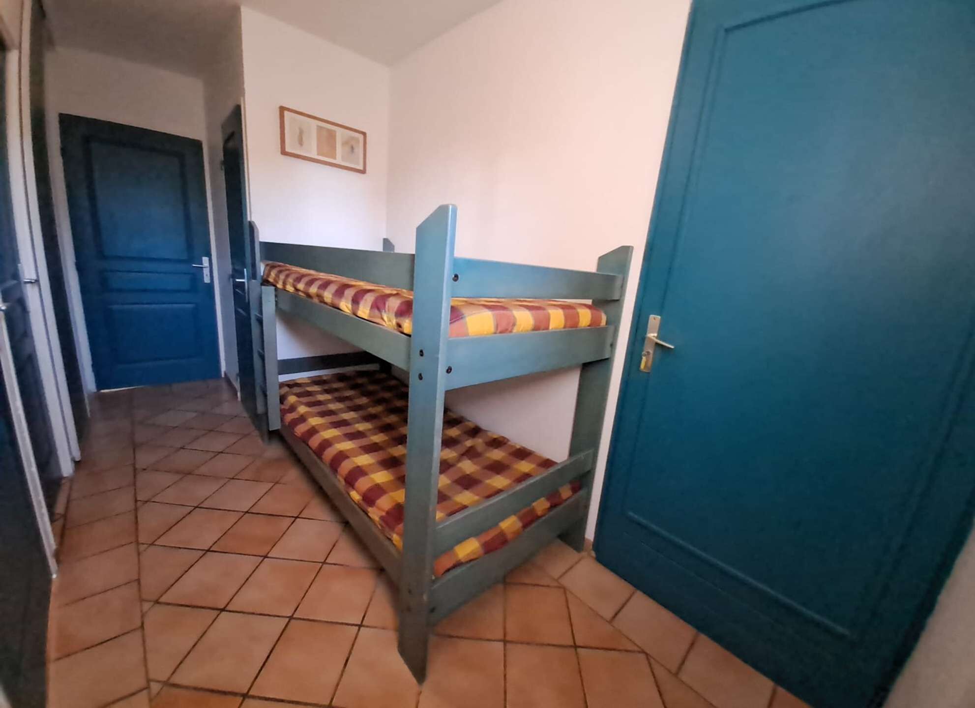 Una habitación con literas, una puerta azul y suelo de baldosas.