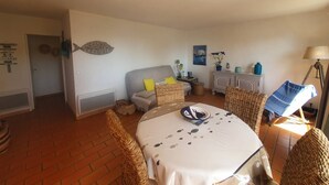 A cozy room with a bed, a dining table, wicker chairs, a cabinet, and a lamp. - Residence with swimming pool, 2 bedroom apartment with east facing terrace, full sea view (ST MANDRIER SUR MER)