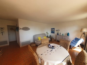 Ein gemütliches Zimmer mit einem Bett, einem Esstisch, Korbstühlen, einem Schrank und einer Lampe.