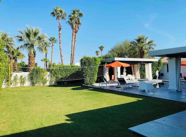 A modern outdoor patio area with a pool, lounge chairs, and a covered seating area.