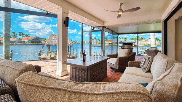 A spacious balcony with wicker furniture, a bar area, and a view of a waterfront with thatched structures. - VRCC Villa Jelly Key, a boaters dream in paradise (Cape Coral)
