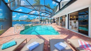 A pool area with a glass-enclosed structure, lounge chairs, and a view of the water. - VRCC Villa Jelly Key, a boaters dream in paradise (Cape Coral)