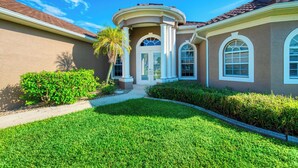 A two-story house with a curved entrance, a covered porch, and a well-maintained lawn. - VRCC Villa Sunny Haven (Cape Coral)