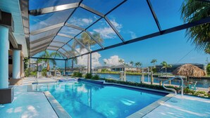 A swimming pool with a clear view of the water, surrounded by palm trees and a thatched-roof structure. - VRCC Villa Sunny Haven (Cape Coral)
