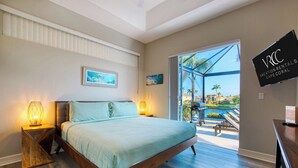 A bedroom with a bed, two bedside lamps, a painting, a sliding glass door leading to a pool area, and a sign for vacation rentals. - VRCC Villa Sunny Haven (Cape Coral)