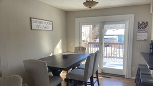 Un coin repas avec une table en bois et quatre chaises, un luminaire au plafond et une porte-fenêtre coulissante donnant sur une terrasse.