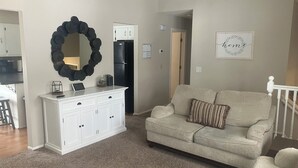 Un salon avec un canapé beige, un meuble blanc, un élément de décoration murale circulaire noir et le mot « chez soi » encadré accroché au mur.