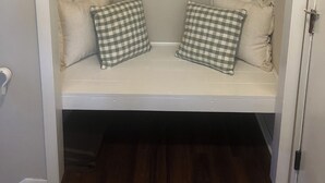 Un banc blanc avec des coussins à carreaux, un porte-manteau au-dessus et une porte sur la droite.