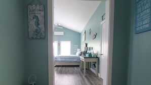 Ein Zimmer mit Türkiswänden, Holzboden, einem Bett, einem Schreibtisch und einer Tür zu einem weiteren Raum.