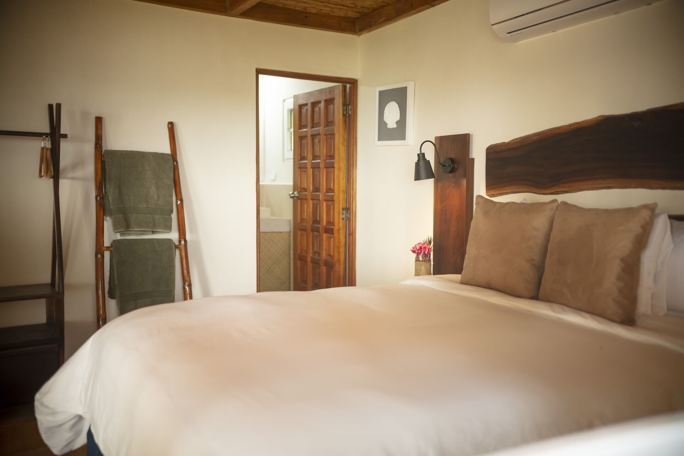 Une chambre à coucher avec un grand lit, une tête de lit en bois, une échelle en bois, un porte-serviettes et une porte donnant sur une autre pièce.
