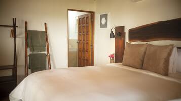 Une chambre à coucher avec un grand lit, une tête de lit en bois, une échelle en bois, un porte-serviettes et une porte donnant sur une autre pièce.