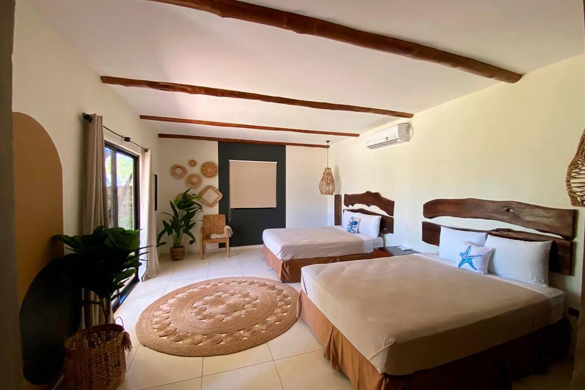 Une chambre avec deux lits, un grand tapis tissé, un plafond en bois et une fenêtre avec des rideaux.