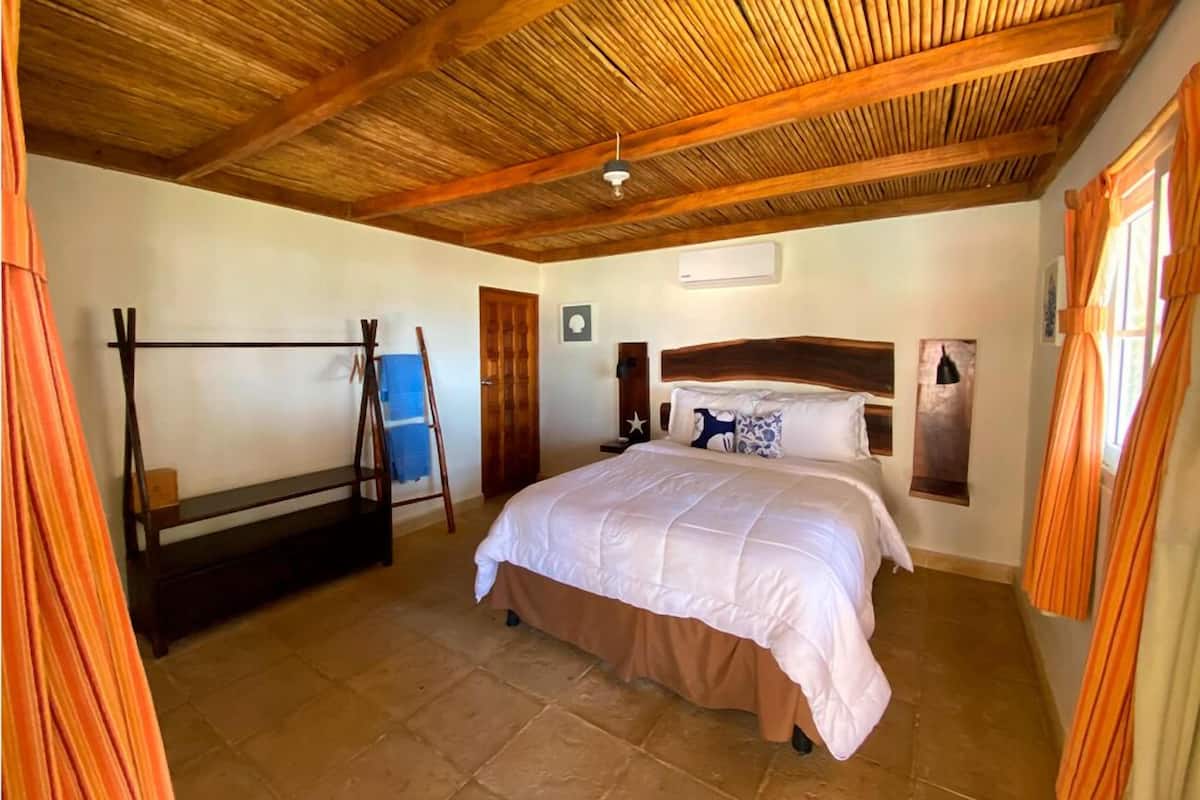 Une chambre avec un plafond en bois, un lit avec une tête de lit, un banc et un appareil de climatisation fixé au mur.