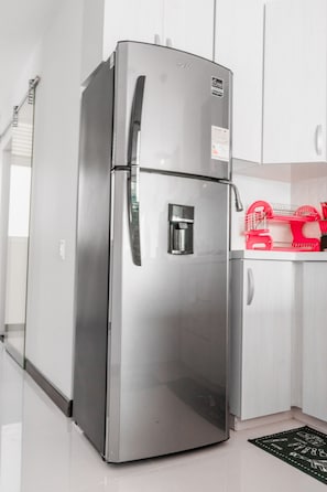 A stainless steel refrigerator in a kitchen with white cabinets and a black and white patterned rug.
