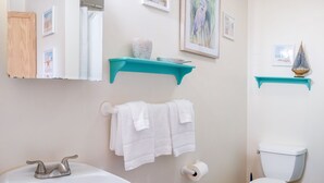 A bathroom with a white sink, a toilet, and a mirror. There are two white towels hanging on the wall, and a framed picture above the sink.
