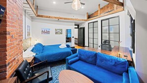 A modern room with two beds, a blue sofa, a wooden table, and a brick wall. - Sleeps 14 · Historic 4BR · Steps to Shaw Metro (Washington)