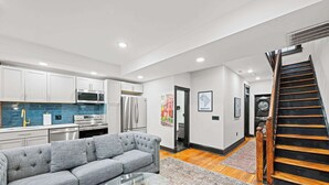 A modern kitchen with white cabinets, a gray sofa, and a glass coffee table. - Sleeps 14 · Historic 4BR · Steps to Shaw Metro (Washington)