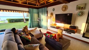 Una sala de estar con un televisor grande, un sofá y una mesa de centro. Se ve una ventana con cortinas y vistas al exterior.