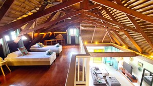 Un amplio dormitorio en ático con vigas de madera, dos camas, un sofá y un televisor.