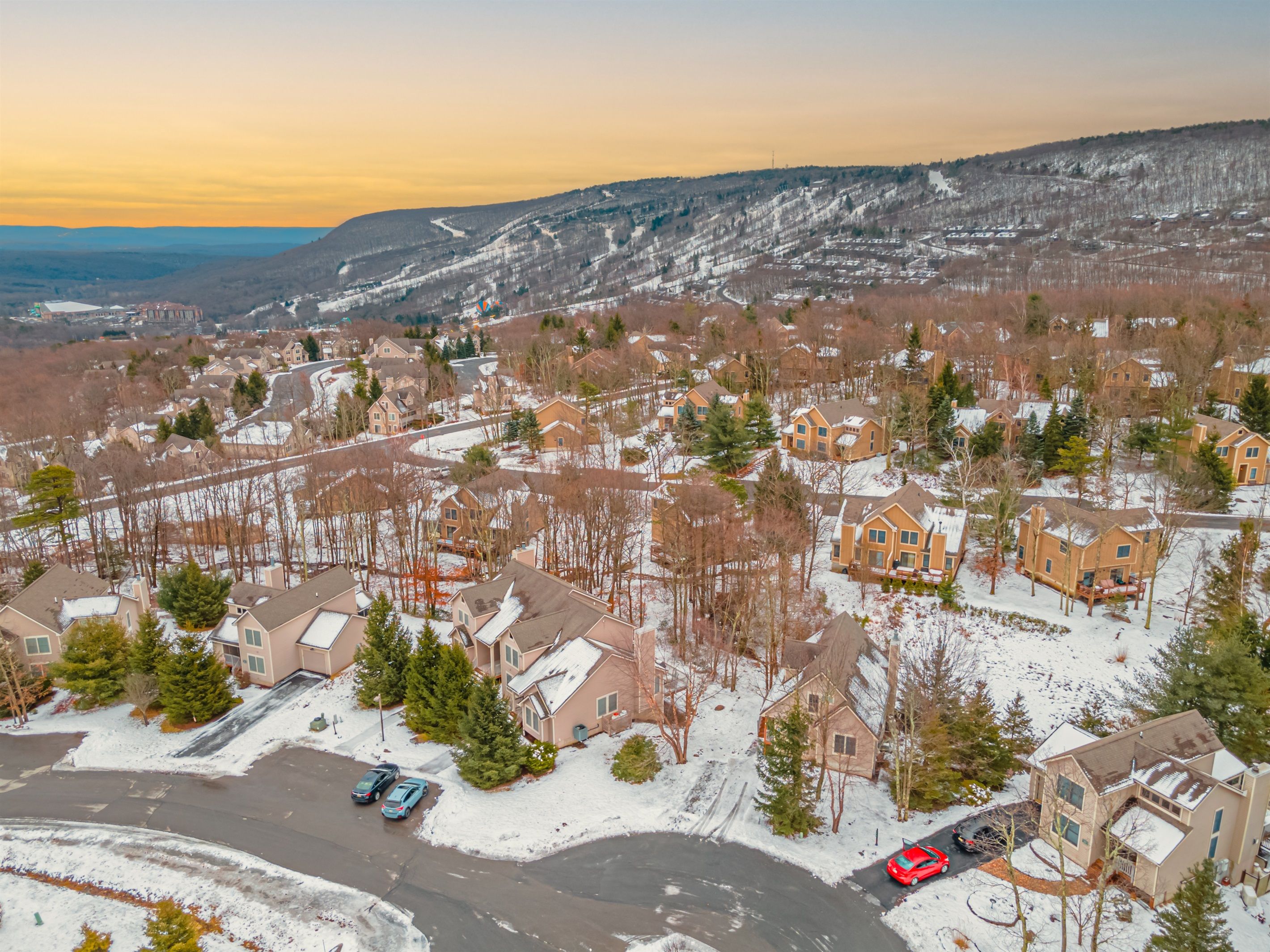 A residential area with snow-covered houses, a parking lot, and a hilly landscape in the background.