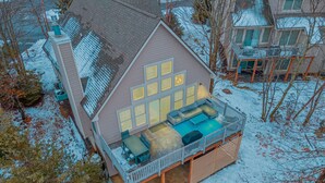 A two-story house with a covered patio area featuring a sofa and a dining table. - Hot Tub, Sauna & Game Room, Sleeps 8, Pet OK - Near Camelback (Tannersville)