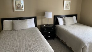 Una habitación de hotel con dos camas, una mesita de noche con lámpara y dos cuadros enmarcados en la pared.