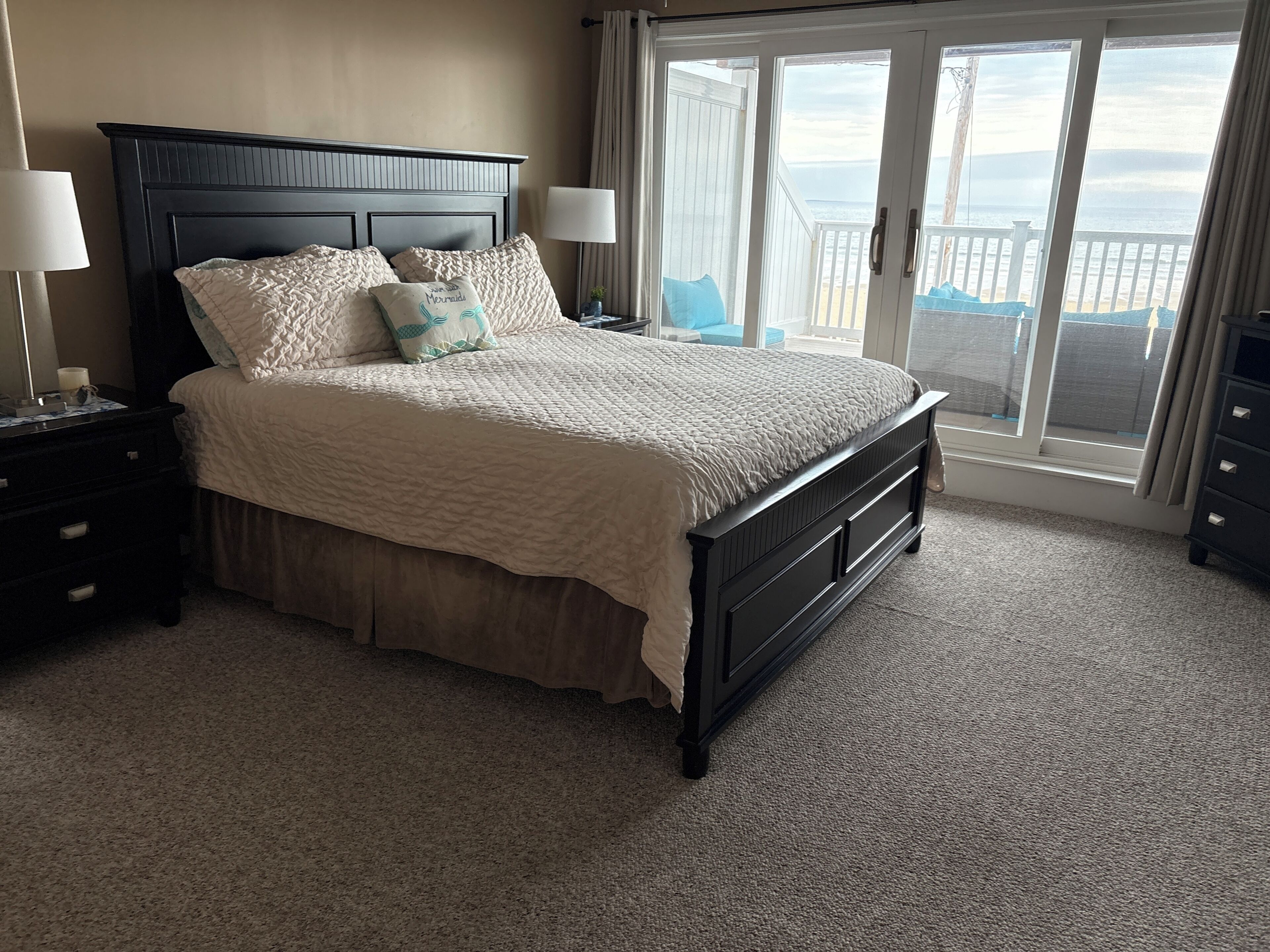 A bedroom with a bed, nightstands, a dresser, and a view of the ocean through a sliding door.