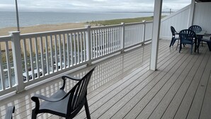 Una terraza techada con vista a la playa, barandillas blancas y mobiliario exterior.