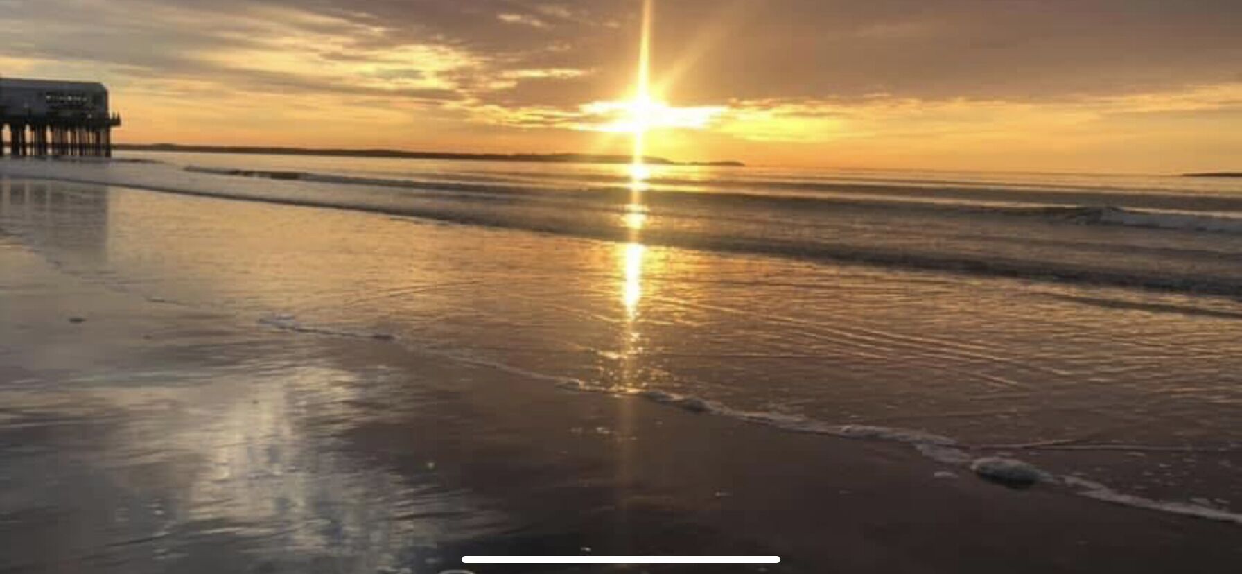 Eine Strandansicht, im Hintergrund ein Steg.