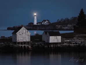 A lighthouse and a house on a rocky shore with calm water in the foreground. - Direct ocean views from extra large balcony!  Over 1200 square feet! (Old Orchard Beach)