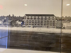 Un hôtel à plusieurs étages, doté d’un toit plat, situé près d’une plage où l’on peut apercevoir de la végétation et d’autres bâtiments.