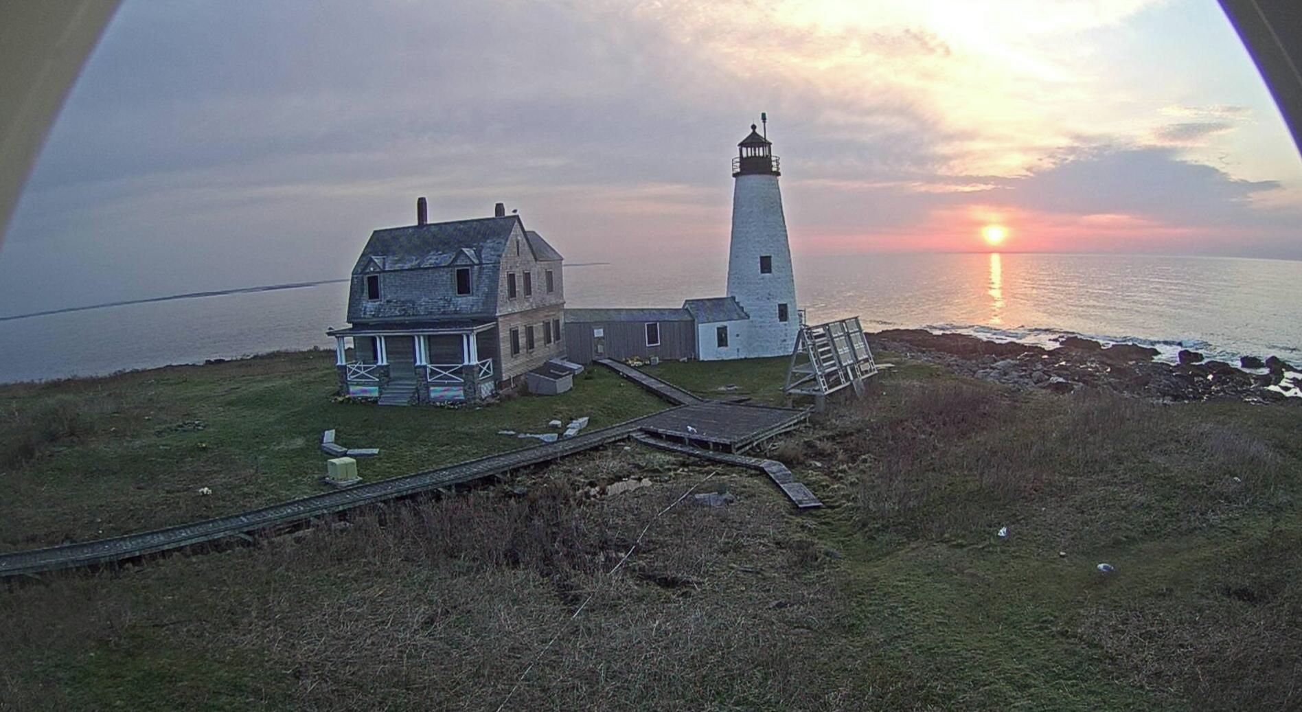 A lighthouse and a house by the sea during sunset.