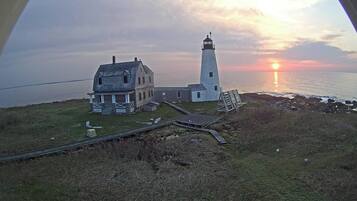 A lighthouse and a house by the sea during sunset.