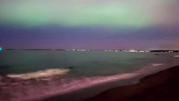 Una playa de noche con vista al océano y un horizonte urbano a lo lejos.