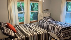 A bedroom with two beds, a ceiling fan, and windows with curtains.