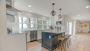 Une cuisine moderne avec des meubles blancs, des appareils en acier inoxydable et un grand îlot central doté de tabourets.
