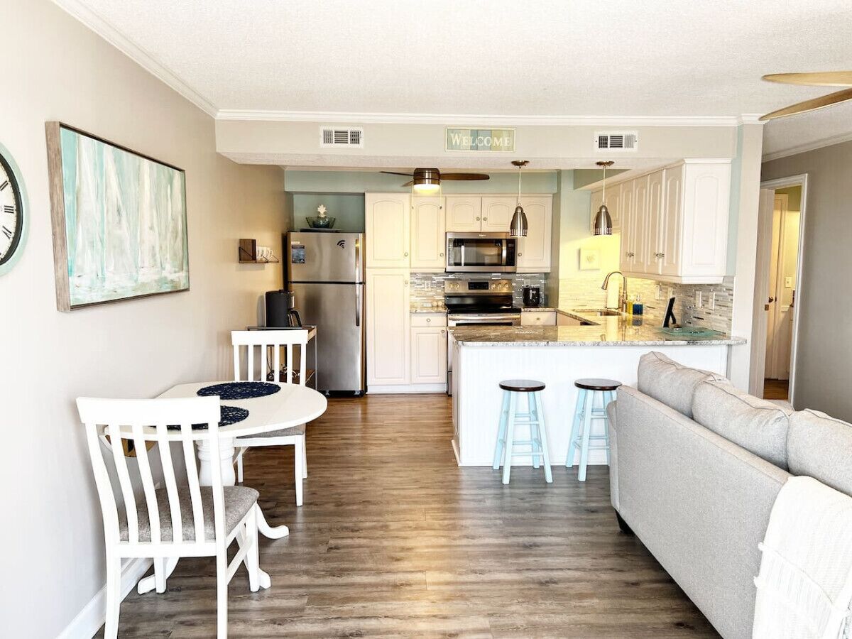 A modern kitchen with white cabinetry, a central island, and a dining area with a white table and chairs.