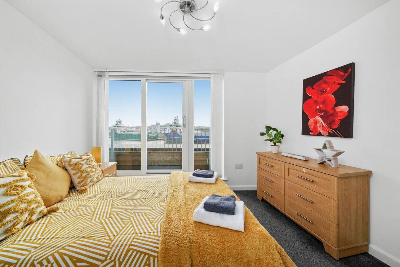 Une chambre moderne avec un grand lit, une commode en bois et un tableau représentant des fleurs rouges.