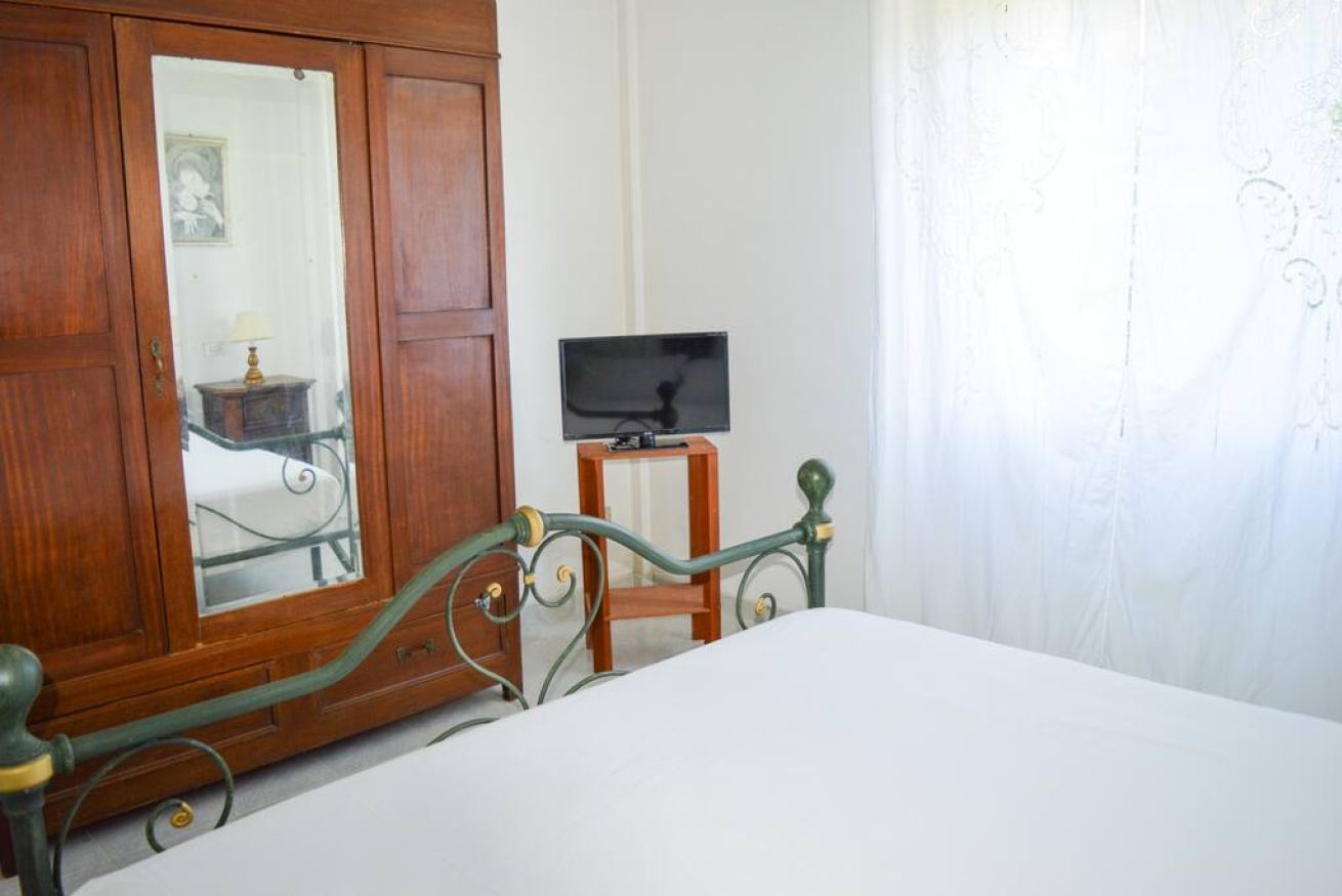 Una camera da letto con un'armadio in legno, una televisione su un piccolo supporto in legno e un letto con lenzuola bianche.