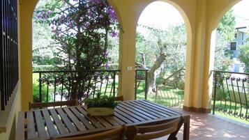 Zona relax all'aperto coperta, con tavolo e sedie, delimitata da un parapetto e affaccio su aree verdi.