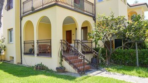 A two-story building with a yellow facade, a balcony with a wrought iron railing, and a staircase leading to the entrance.