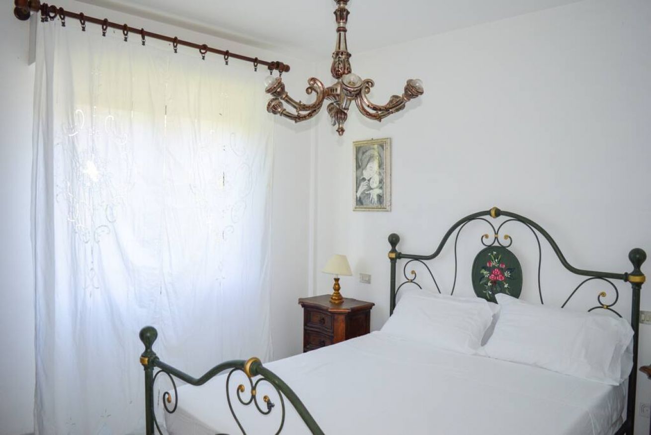 A bedroom with a four-poster bed, a chandelier, a nightstand with a lamp, and a framed picture on the wall.