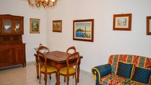 A dining area with a wooden table and chairs, a colorful sofa, and framed pictures on the walls.