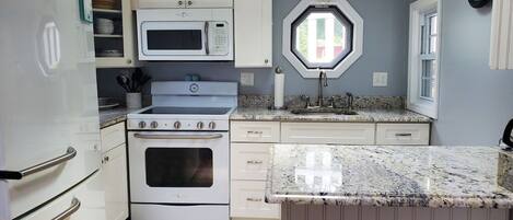 A compact kitchen with white cabinetry, a built-in microwave, a stove, and a sink.