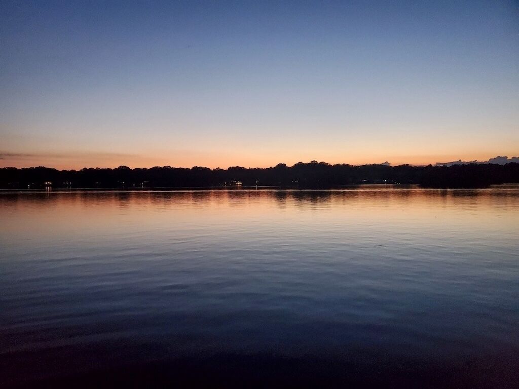 A calm lake at dusk with a clear horizon and distant city lights.