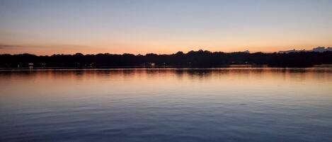 A calm lake at dusk with a clear horizon and distant city lights.