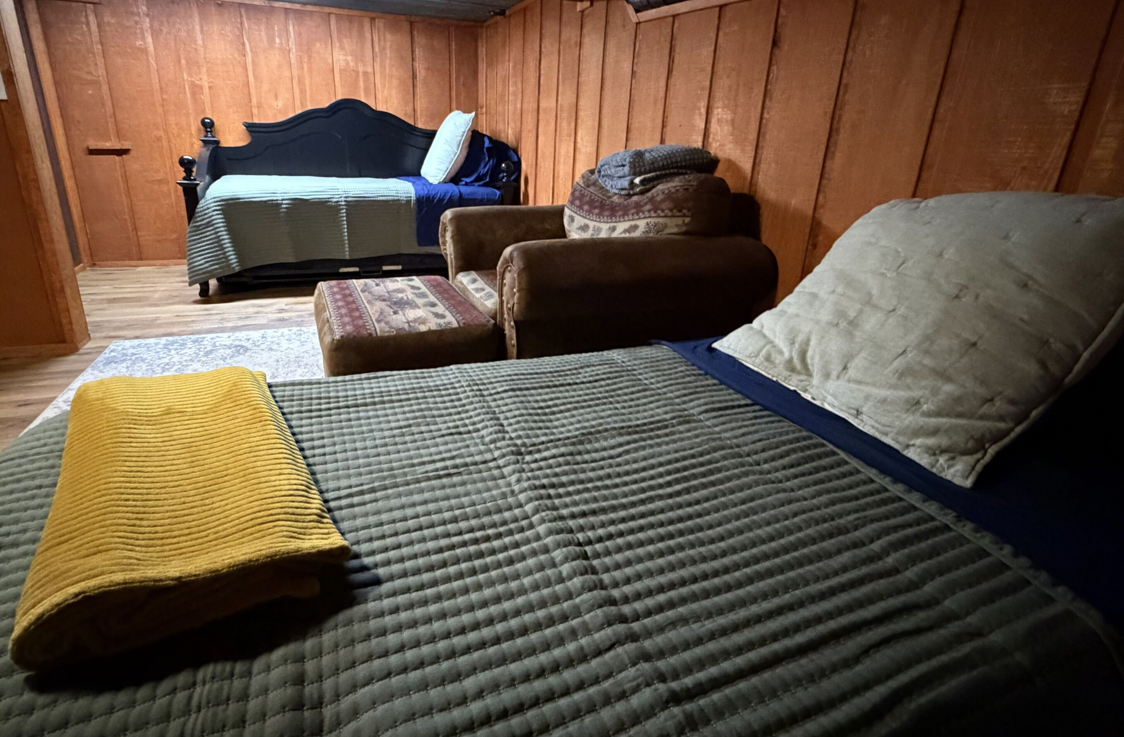 Una habitación con una cama, una silla, una mesita y una pared de madera.
