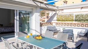 Een terras met een tafel en stoelen, een glazen deur naar een slaapkamer en een decoratieve wand met planten.